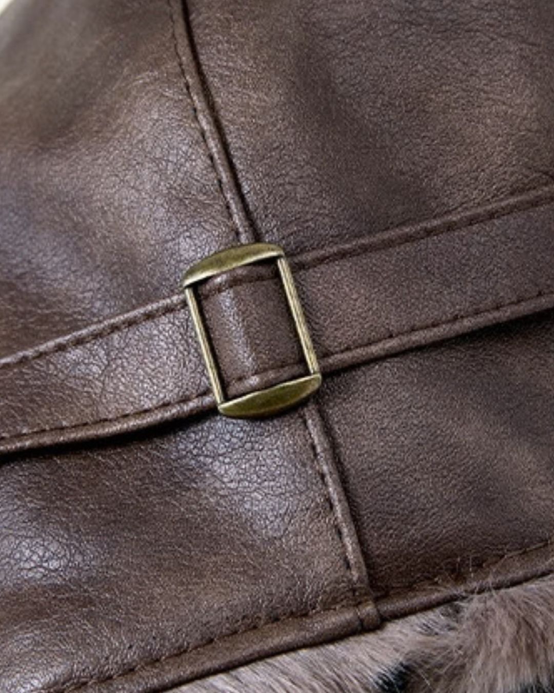 Close-up of a brown leather trapper hat featuring an adjustable brass buckle strap and soft fleece lining on the ear flaps.