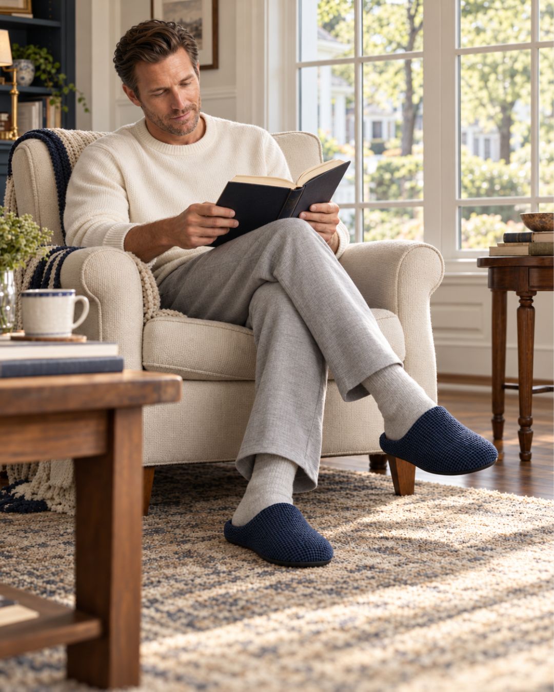 Man wearing navy blue suede plush-lined house slippers with a thick non-slip sole while relaxing in an armchair.