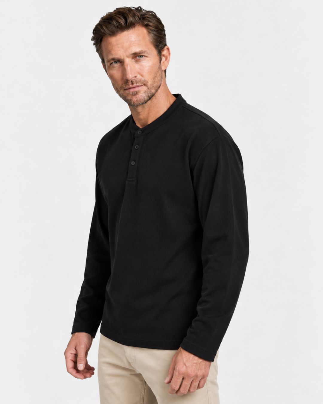 Man wearing a black long-sleeve textured waffle-knit henley shirt with a three-button band collar and dropped shoulders.