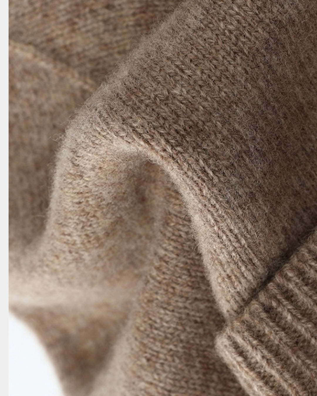 Close-up of a soft, tan wool knit beanie featuring a ribbed fold-over cuff and textured fabric detail.