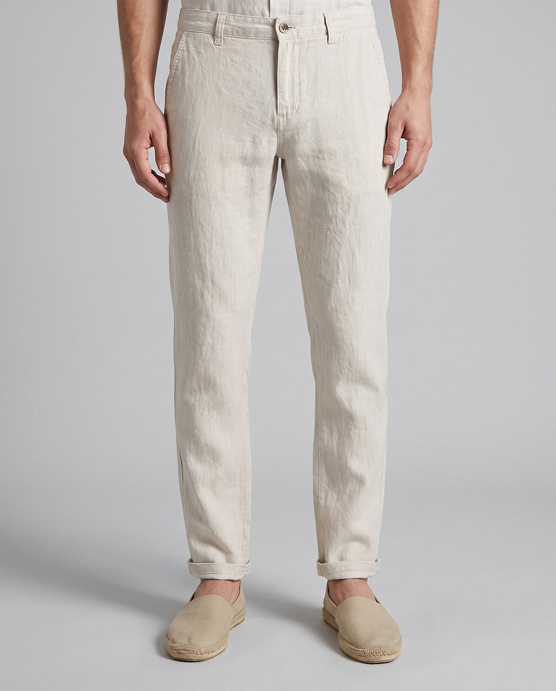 A person wearing light beige linen trousers and matching slip-on shoes, shown from the waist down against a plain light gray studio background.