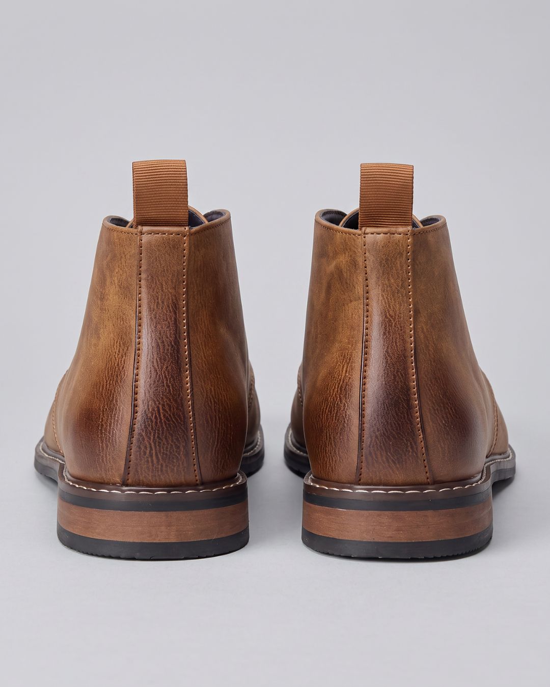 A pair of tan leather ankle boots shown from the back, featuring a pull tab at the top of each boot and a stacked sole with a black outsole, by Hudson & Tate.