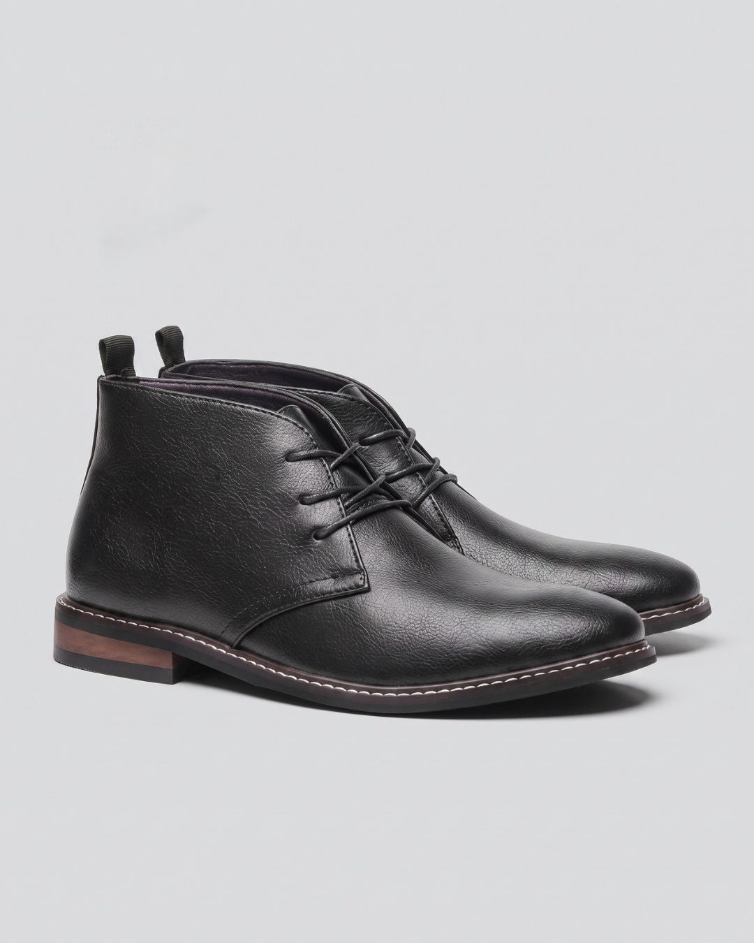 A pair of men's black leather chukka boots with laces, shown from a three-quarters angle by Hudson & Tate.