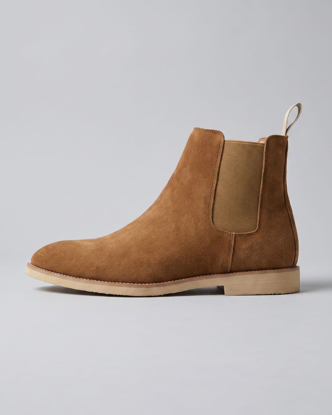 A single tan suede Chelsea boot with elastic side panels and a low stacked heel, shown in profile against a light gray studio background.