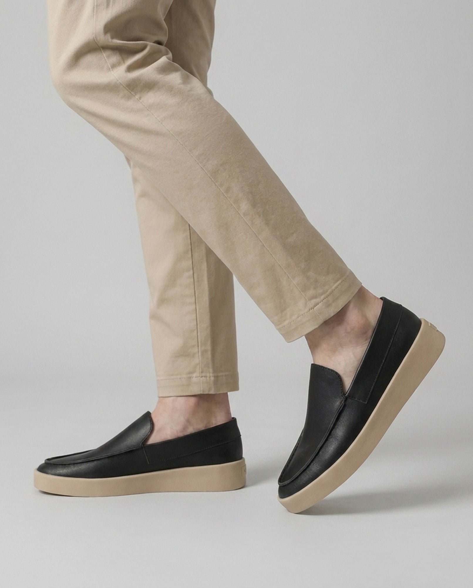 Boston men's black slip-on loafers styled with beige chinos on grey background