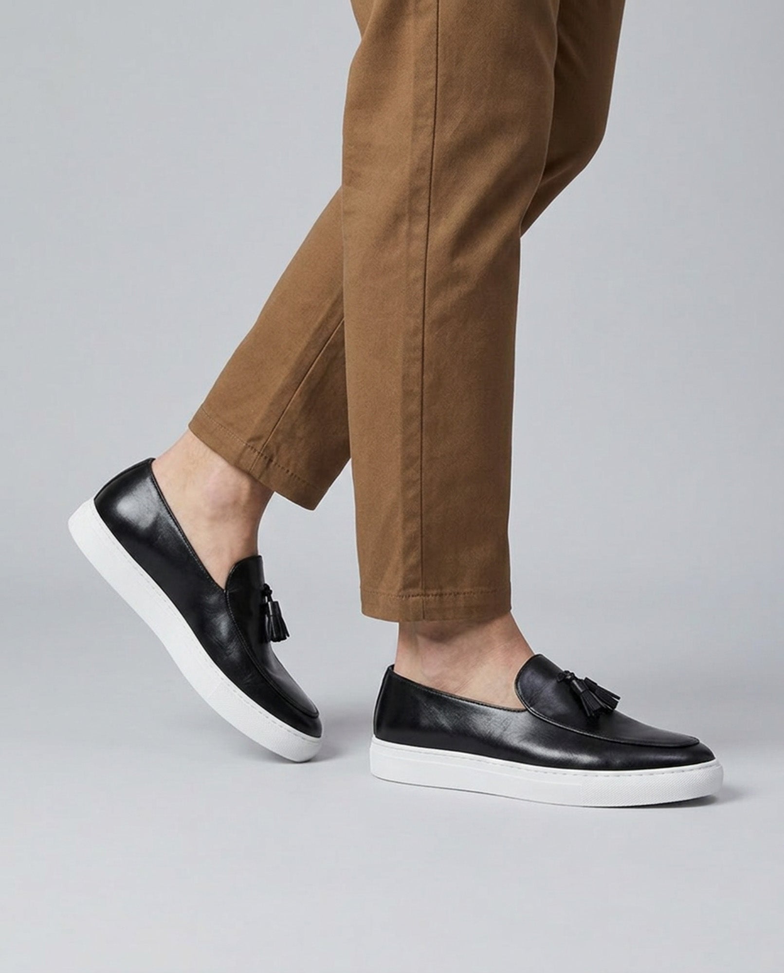 Capri men's black leather tassel loafers mid-stride styled with tan chino trousers