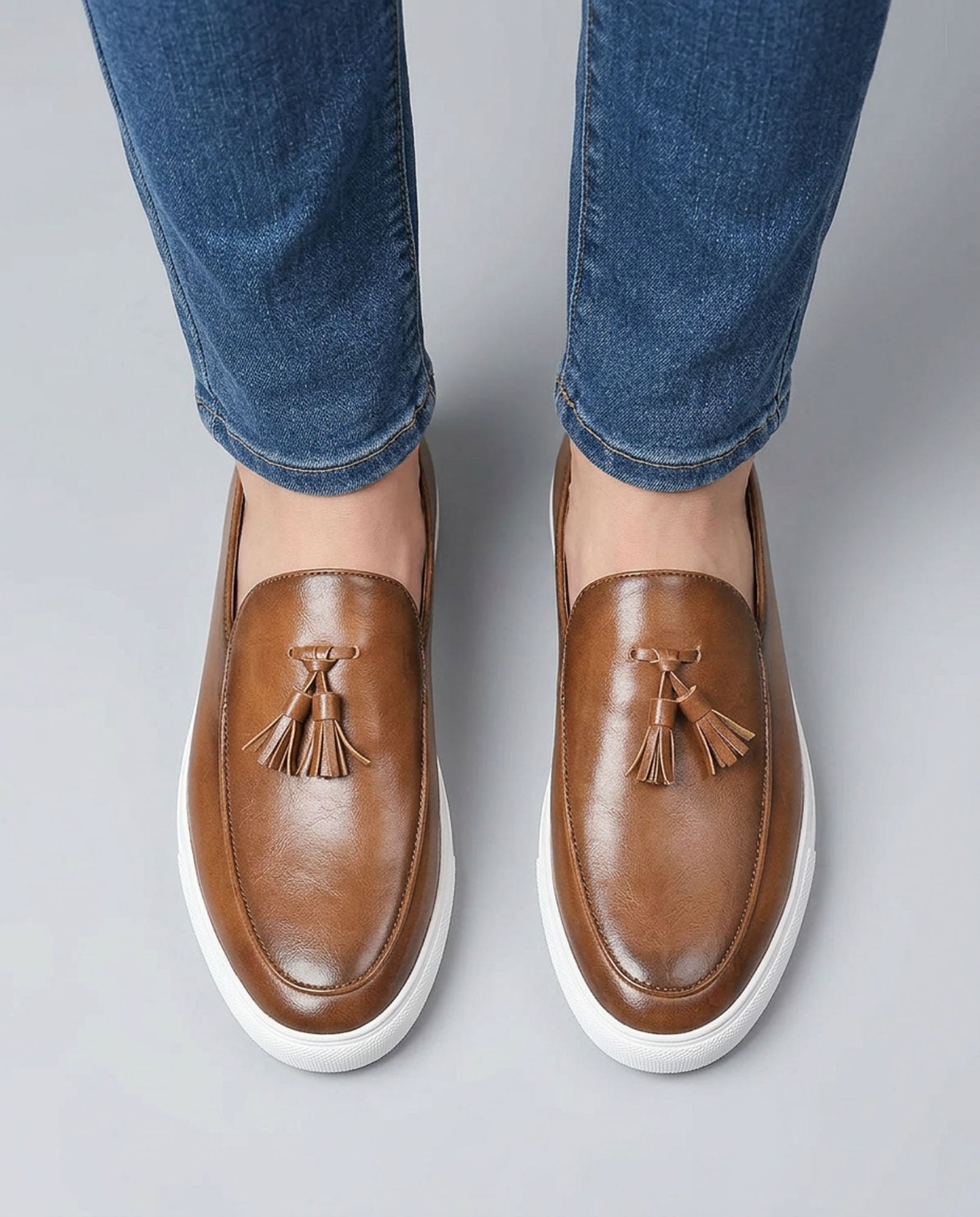 Overhead view of Capri men's cognac leather tassel loafers with white cupsole styled with blue denim