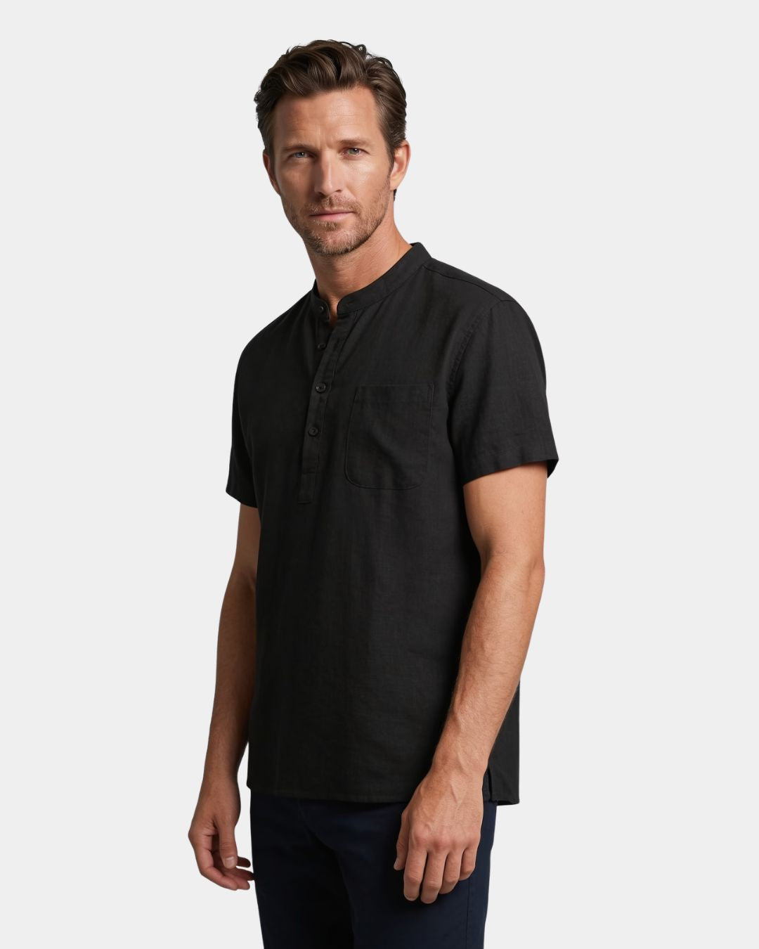 A man wearing a black short-sleeve henley shirt with a chest pocket, photographed against a light gray studio background.