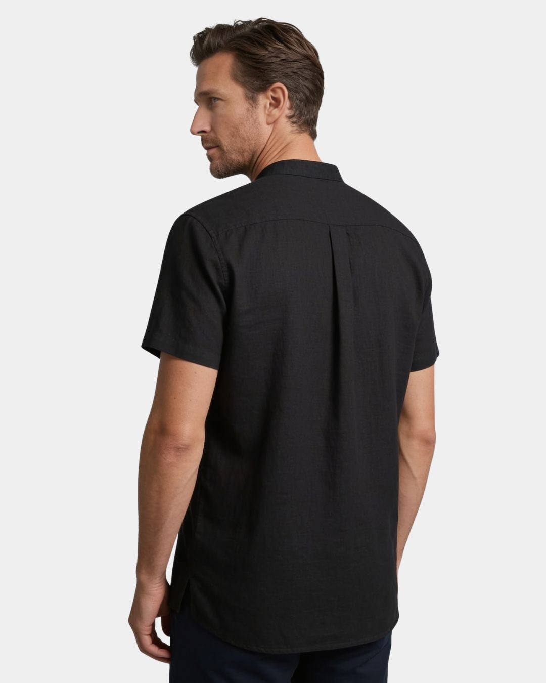 A man wearing a black short-sleeve button-up shirt, shown from the back against a light gray studio background.