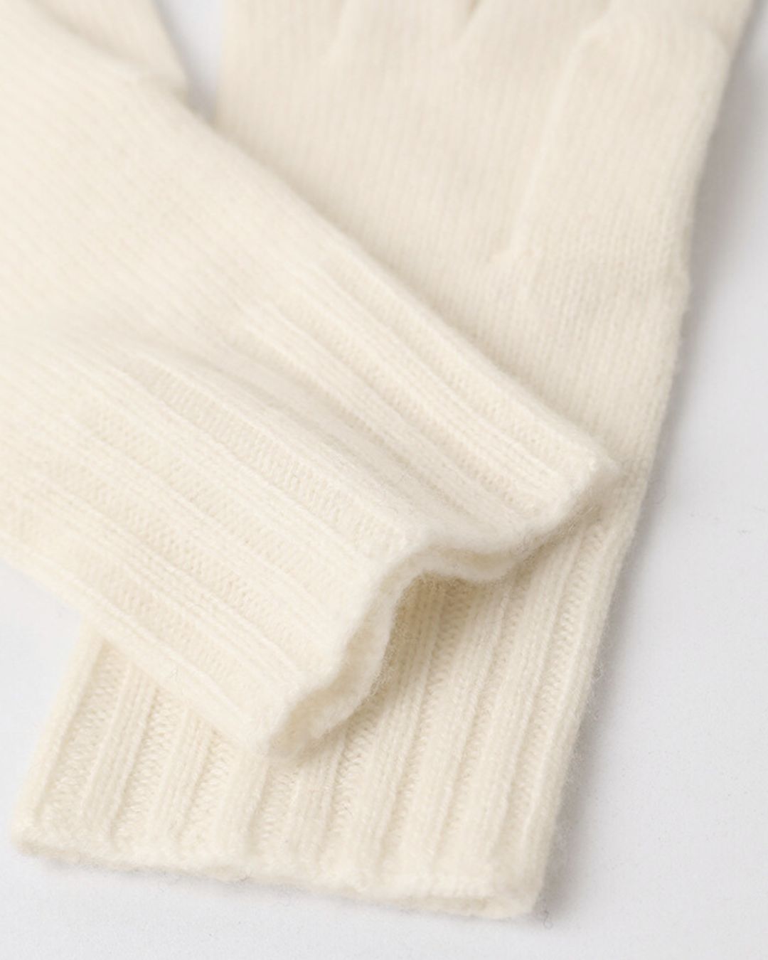 Cream-colored cashmere gloves featuring a soft, ribbed knit texture for a refined winter look.