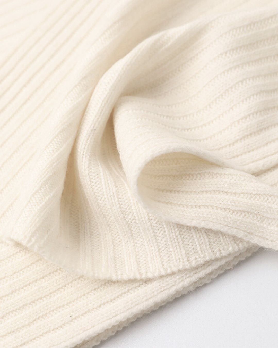 Close-up of a soft, cream-colored ribbed cashmere knit fabric from a winter scarf and hat set.