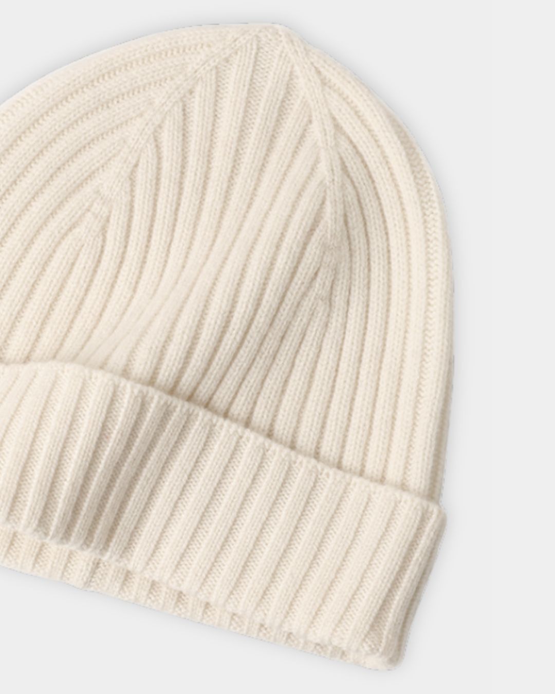 Cream-colored cashmere beanie with a classic ribbed knit texture and a folded cuff for a warm winter look.