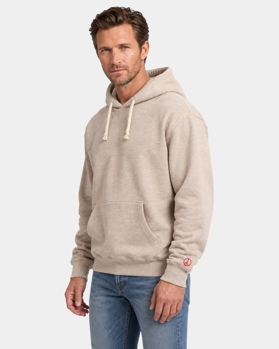Beige oversized cotton pullover hoodie with a drawstring hood, kangaroo pocket, and small red peace symbol on the sleeve.