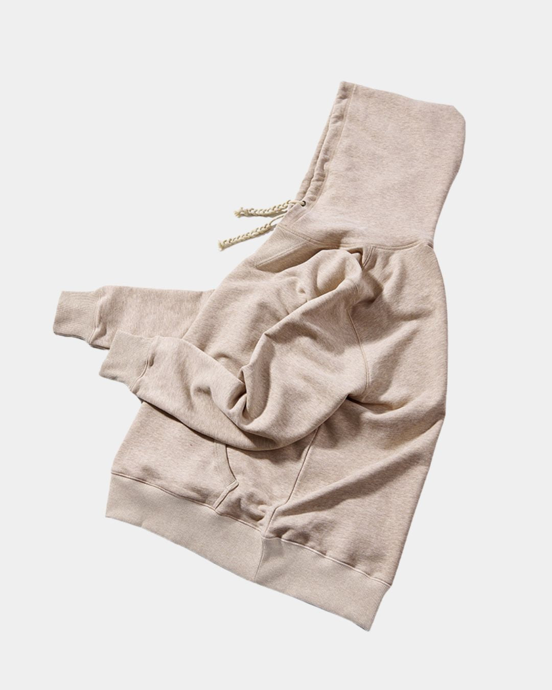 Beige oversized cotton pullover hoodie with a drawstring hood, kangaroo pocket, and ribbed hem on a white background.