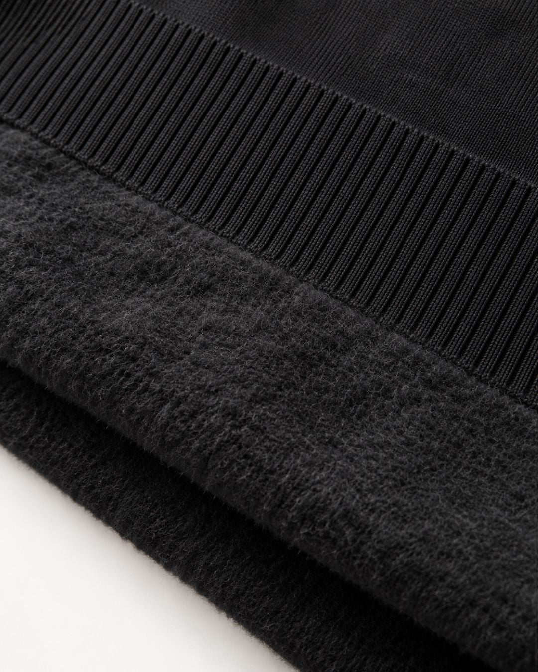 Close-up of a black men's sweater featuring a soft, brushed fleece interior and a structured ribbed knit hem.