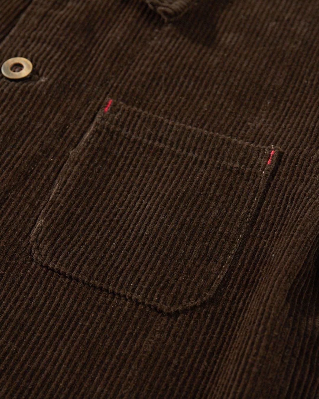 Brown corduroy chore jacket featuring a chest patch pocket with red bar-tack stitching and button front closure.