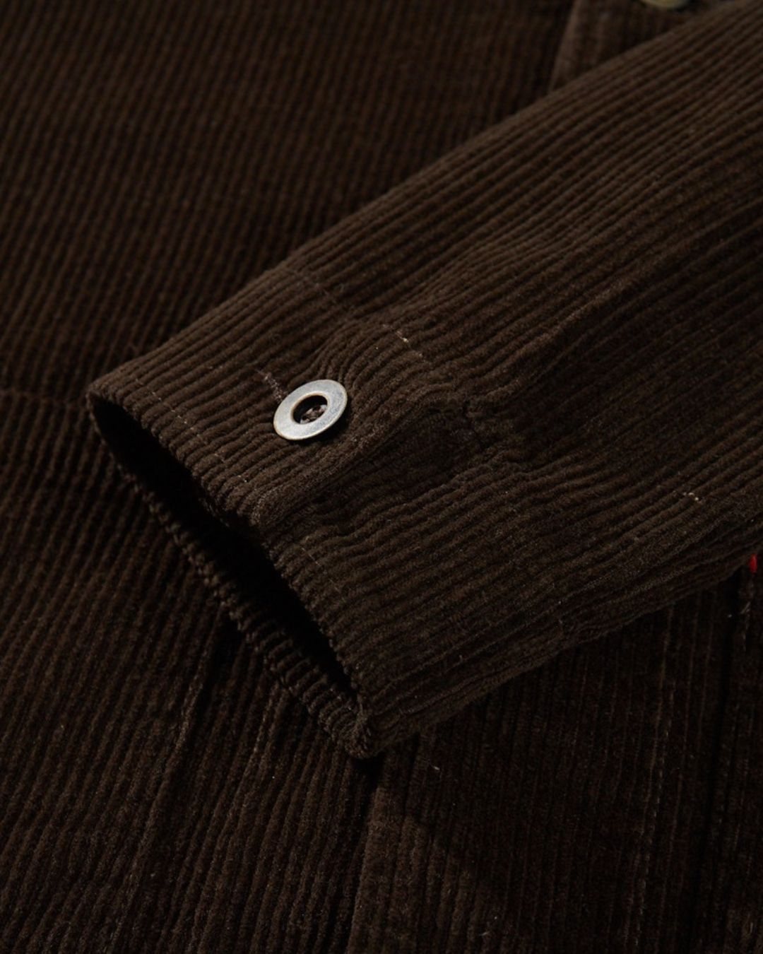 Close-up of a brown ribbed cotton corduroy chore jacket sleeve with a button cuff.