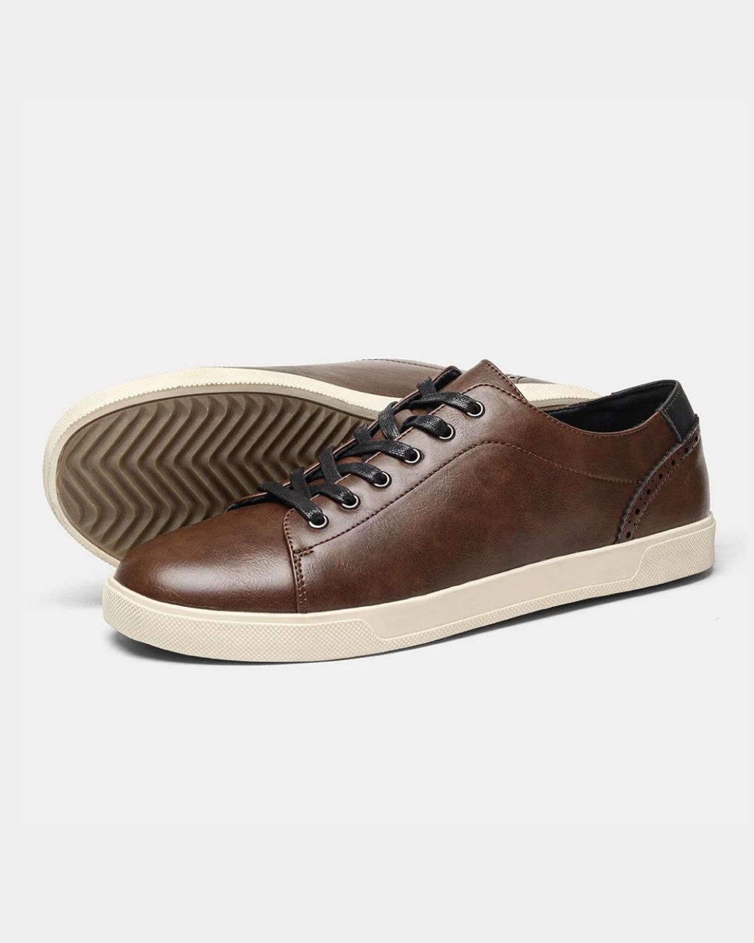 Men’s brown faux leather low top dress sneakers with black laces, brogue heel detailing, and a cream rubber sole.