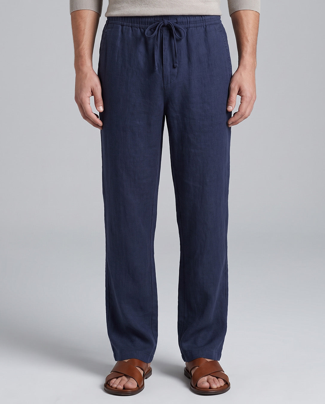 A person wearing navy blue drawstring lounge pants with a light beige top and brown sandals, shown from the waist down against a light gray studio background.