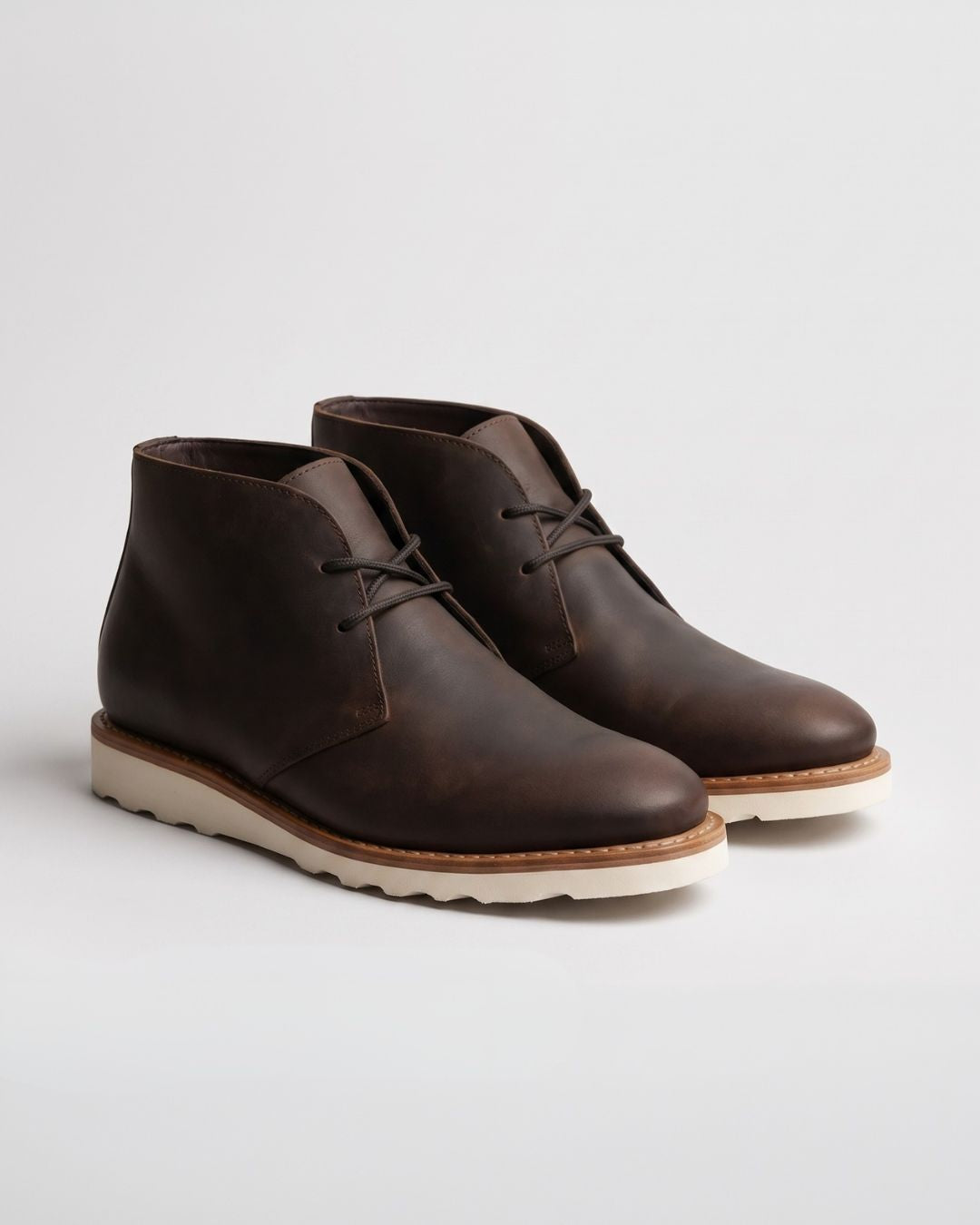 Dark brown faux leather chukka boots with a rounded toe, lace-up ankle design, and a chunky white foam sneaker sole.