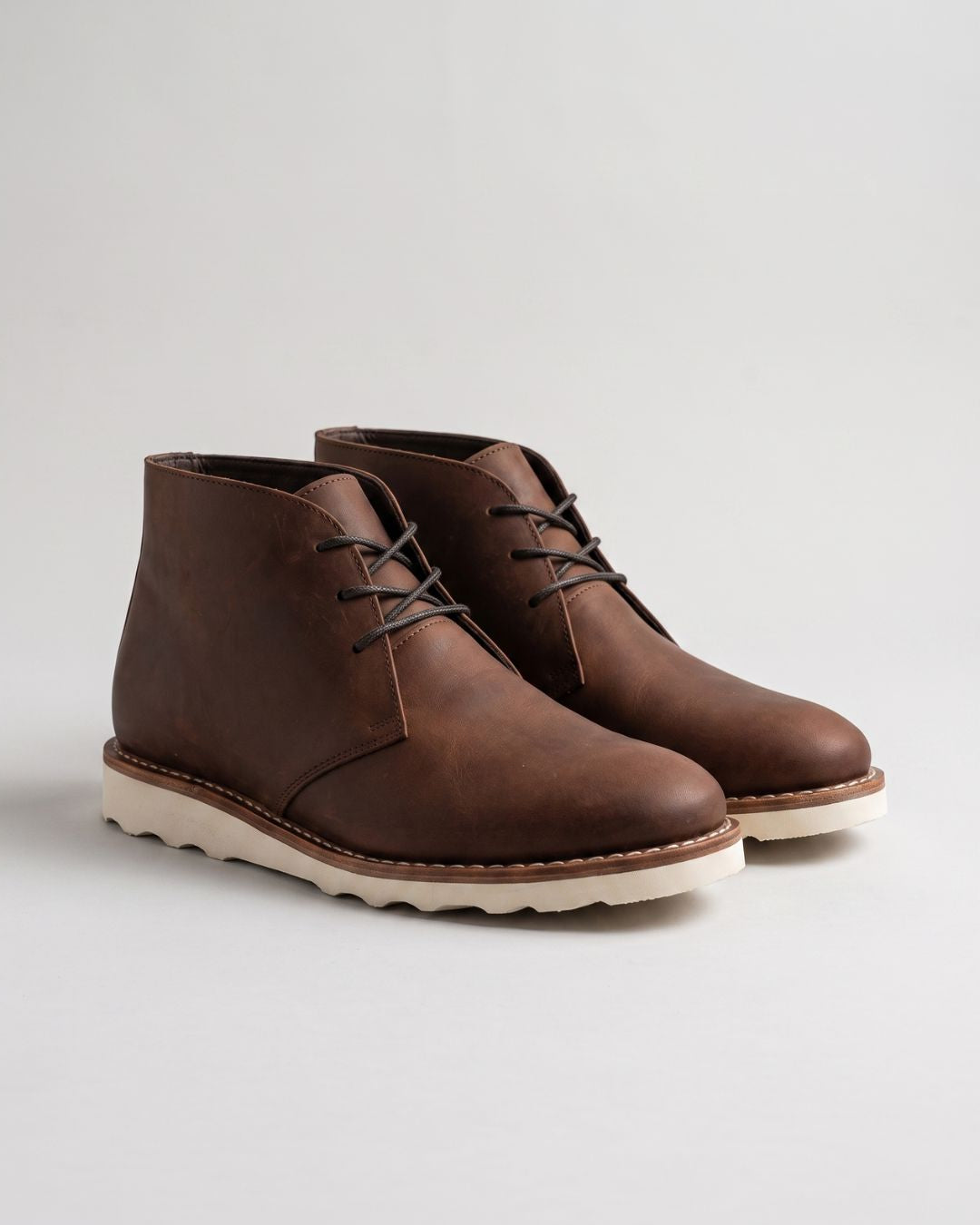 Men's brown faux leather chukka boots with a rounded toe, lace-up closure, and a chunky white foam sneaker sole.