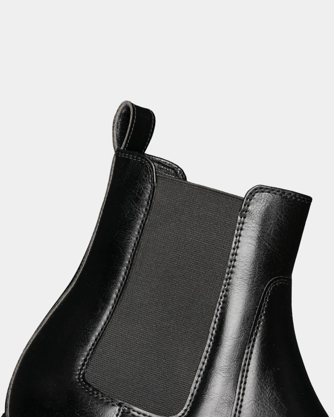 Close-up of a black Chelsea boot featuring smooth textured leather, elastic side panels, and a pull tab.
