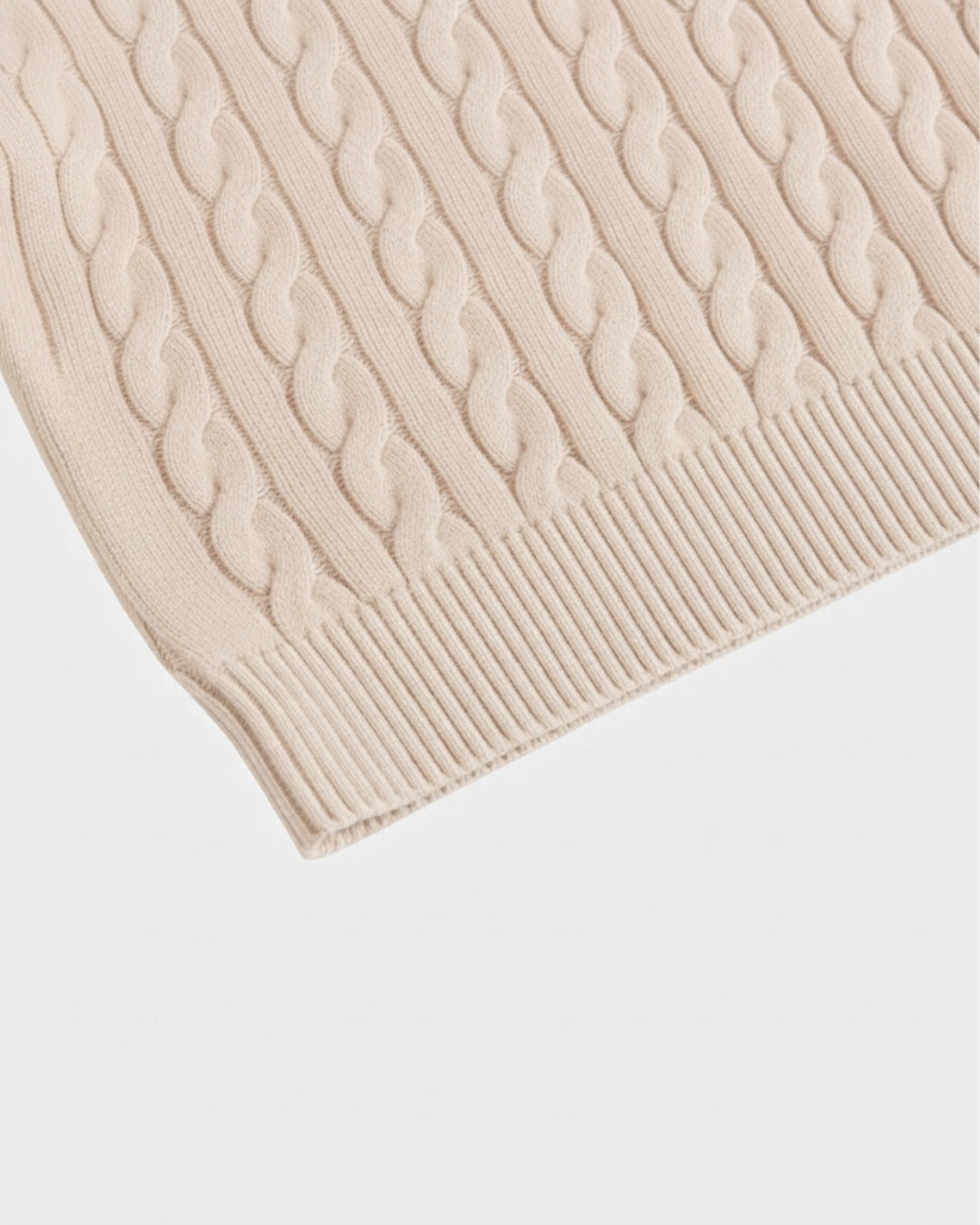 Close-up of a beige cotton cable knit sweater featuring a ribbed hem and textured vertical cable pattern.