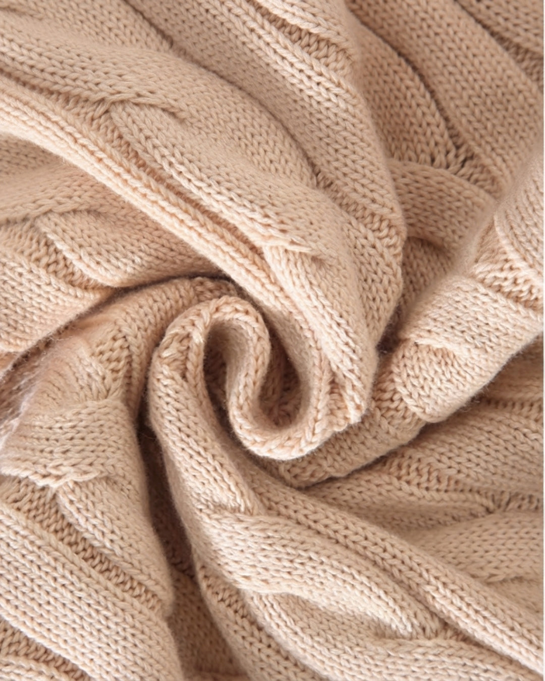 Close-up of a beige 100% cotton cable knit sweater showing the soft, textured fabric weave.