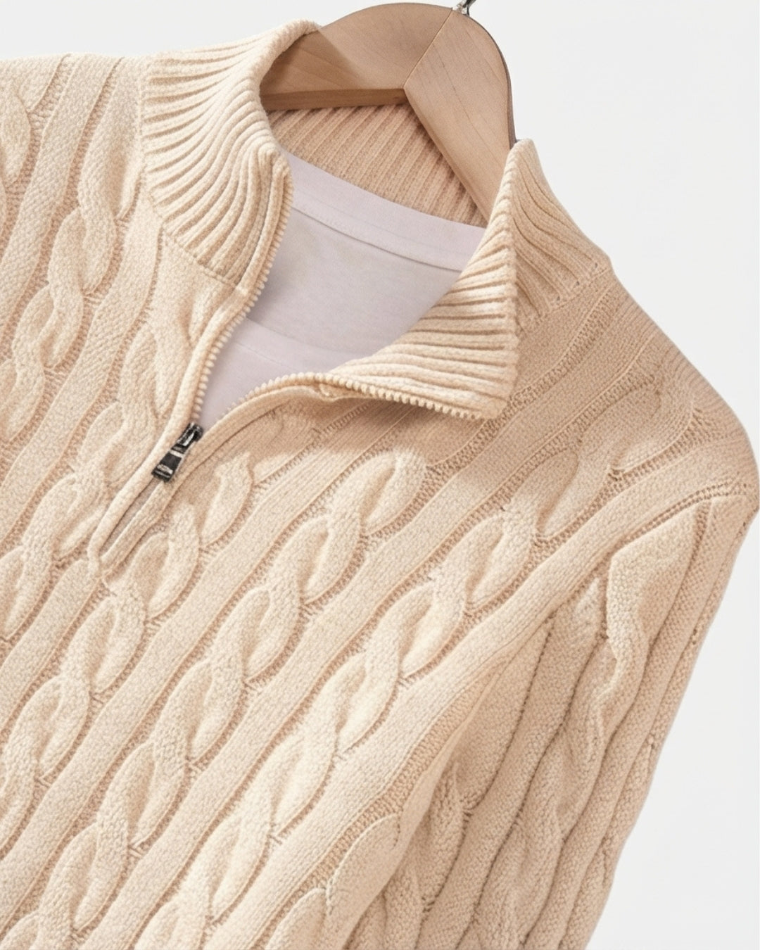 Beige cotton cable knit quarter-zip sweater with a mock-neck collar and ribbed trim on a wooden hanger.