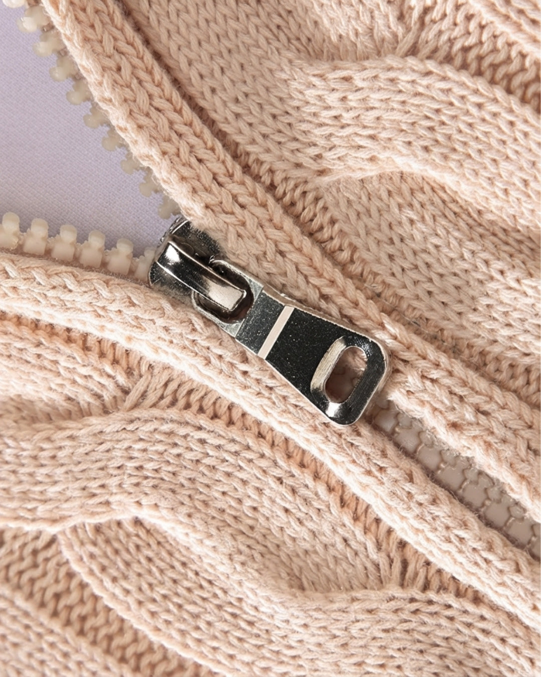 Close-up of a beige cotton cable knit sweater featuring a silver quarter-zip metal pull and textured knit pattern.