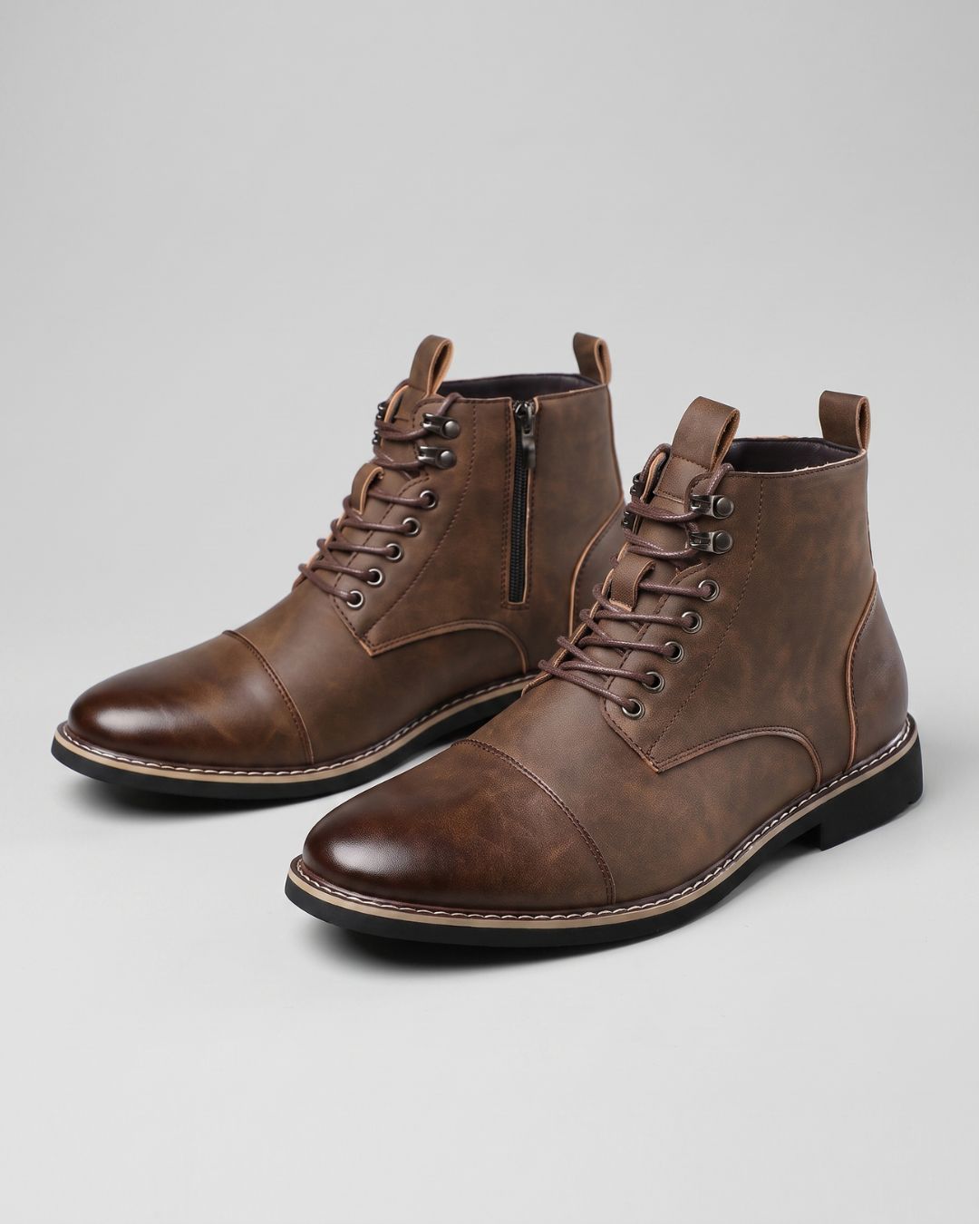 Brown men's cap-toe ankle boots with lace-up front, metal eyelets, and convenient side zipper on a grey background.