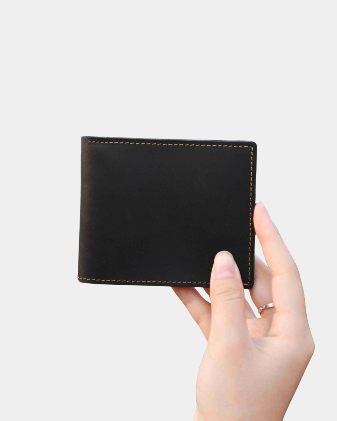Hand holding a compact, dark brown Crazy Horse leather bifold wallet with contrast stitching.