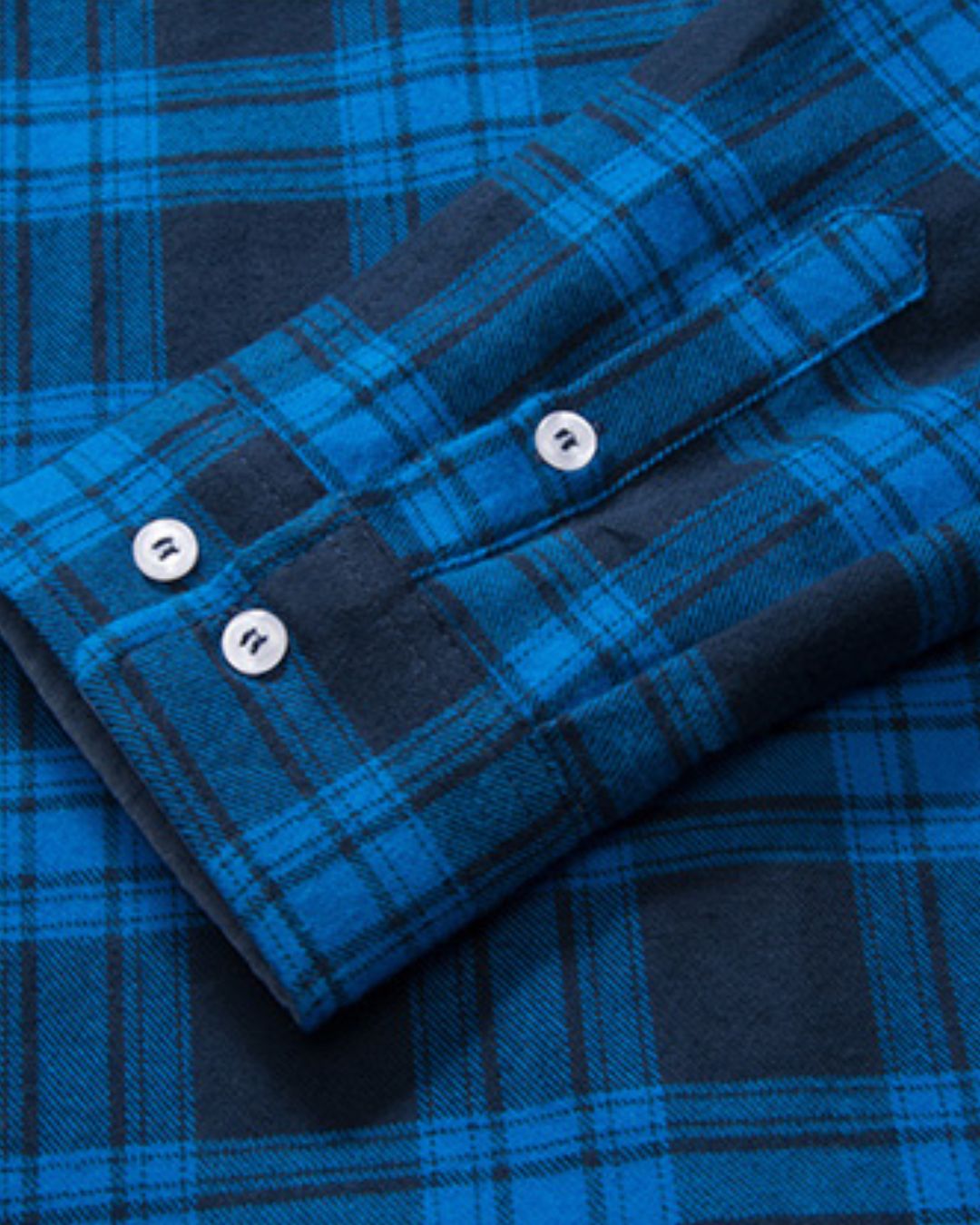 Close-up of a blue and black plaid flannel shirt sleeve with double-button cuffs and soft brushed fabric texture.