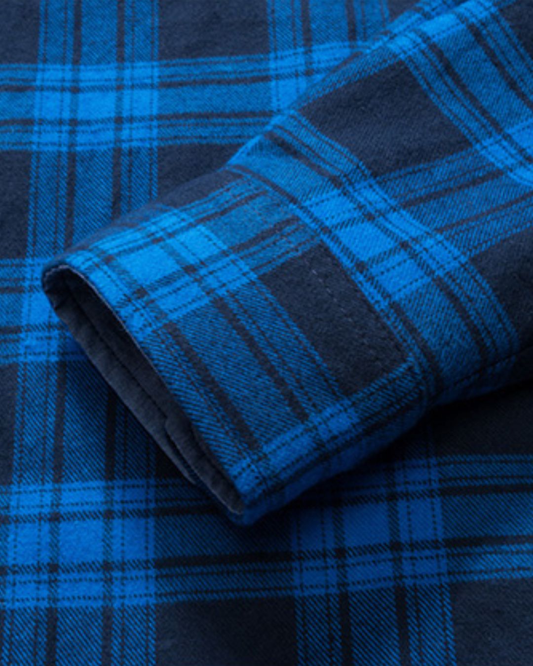 Close-up of a soft, brushed blue and black plaid flannel shirt sleeve with a buttoned cuff.