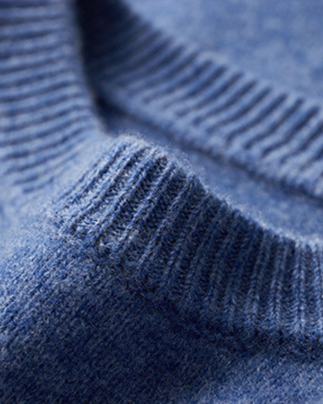 Close-up of a blue men’s crew neck sweater featuring a soft wool knit texture and a ribbed neckline.
