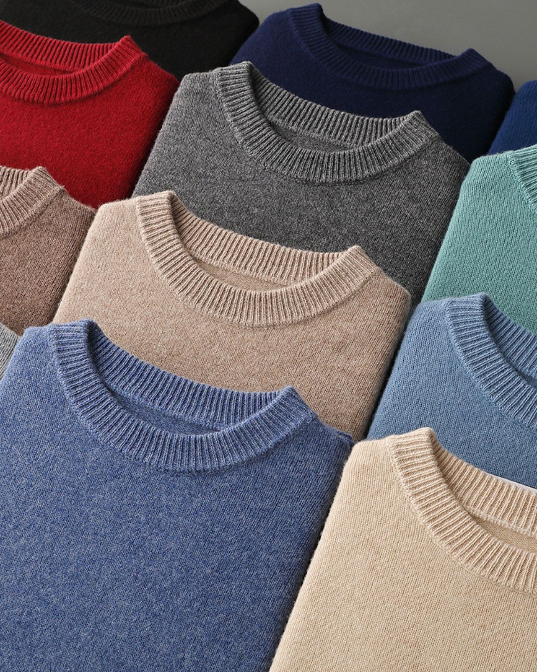 Stack of men’s classic crew neck sweaters in various colors, crafted from soft 100% wool with ribbed necklines.