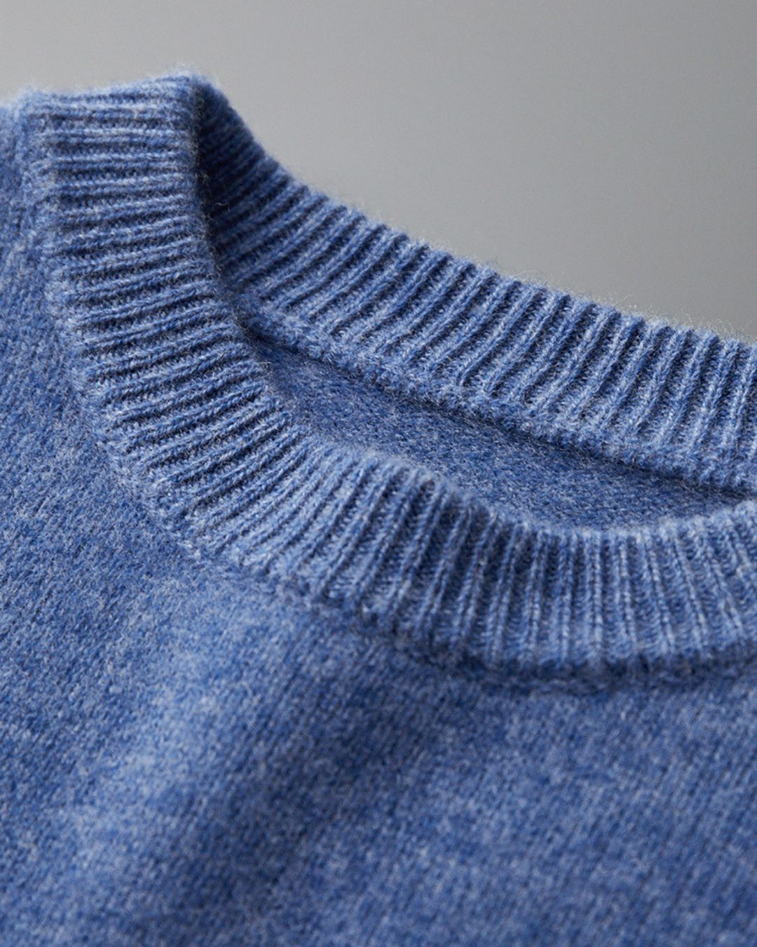 Close-up of a blue men’s crew neck sweater in soft 100% wool with a ribbed neckline and smooth knit texture.