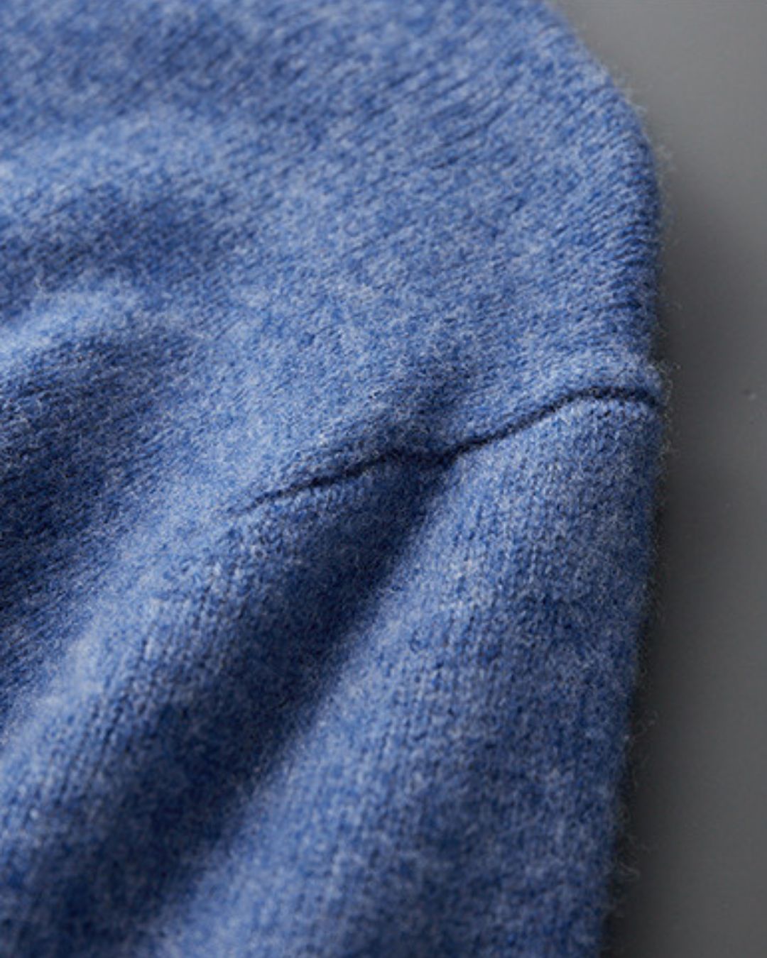 Close-up of a soft blue 100% wool crew neck sweater showing the fine knit texture and shoulder seam detail.