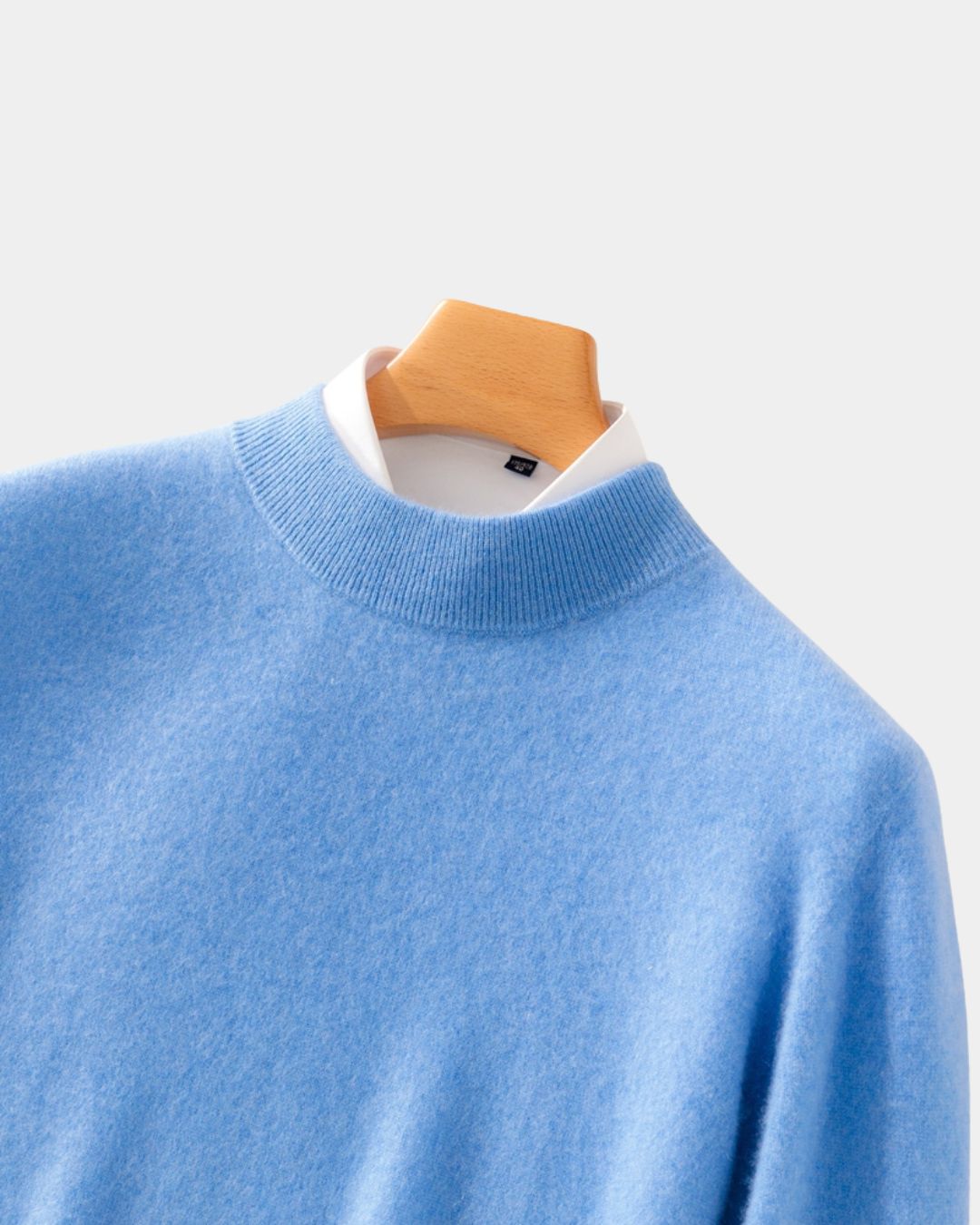Light blue wool mock neck sweater with a ribbed collar layered over a white shirt on a wooden hanger.