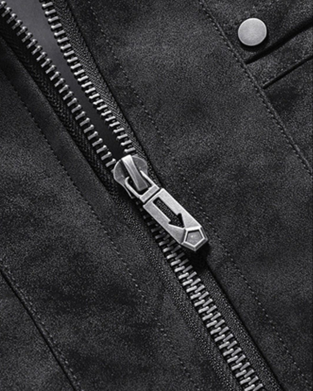 Close-up of a black bomber jacket with a silver metal zipper and a matching silver zipper pull, showing part of a buttoned pocket.