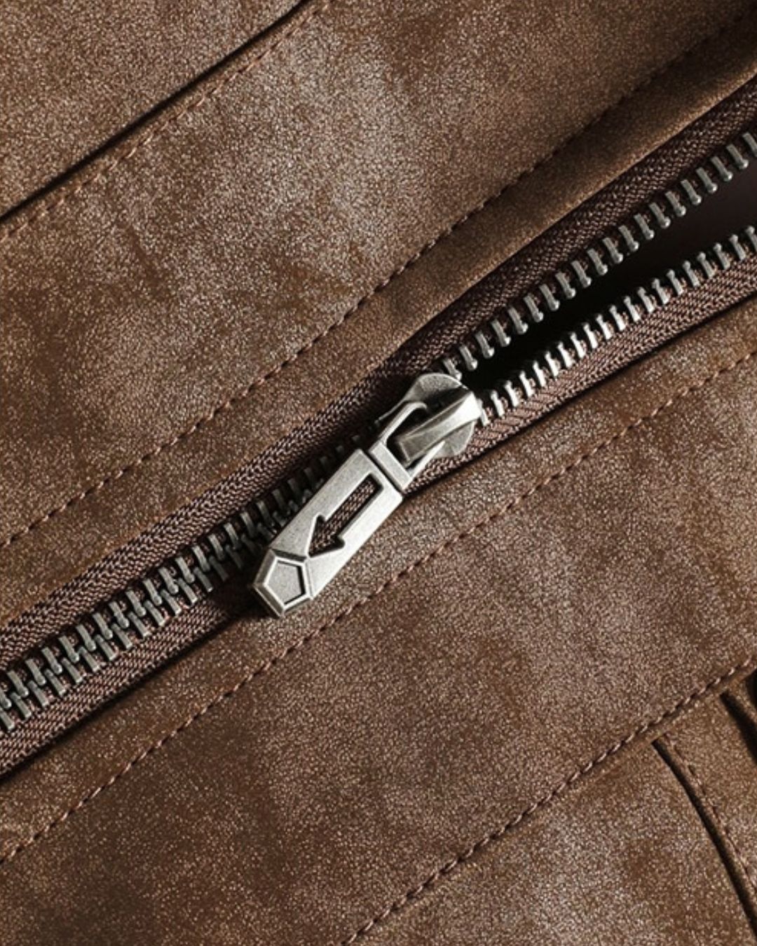 Close-up of a brown bomber jacket and zipper detail with a silver-toned pull tab on a matching brown fabric surface.