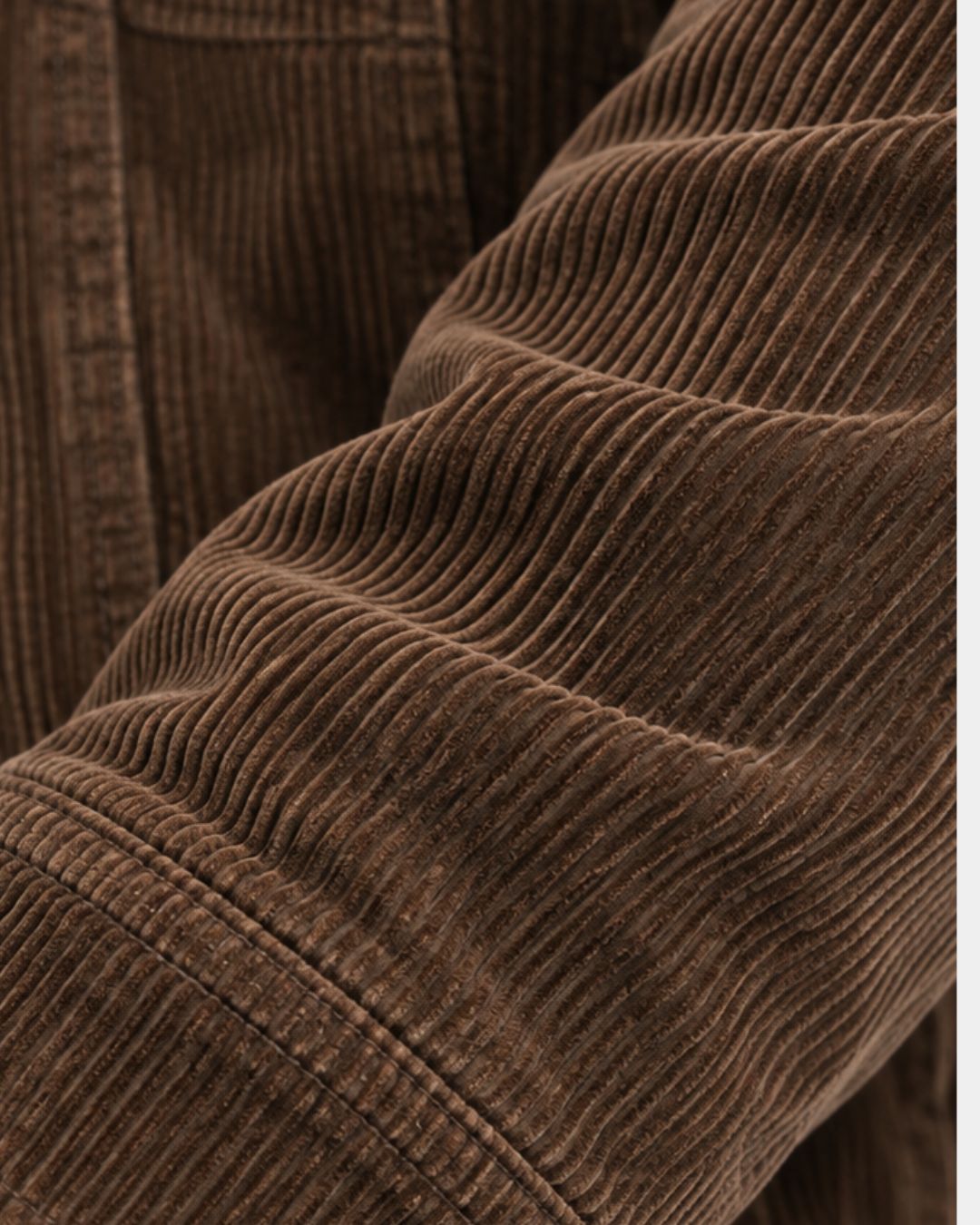 Close-up of a brown corduroy trucker jacket sleeve featuring textured vertical wales and a stitched cuff detail.