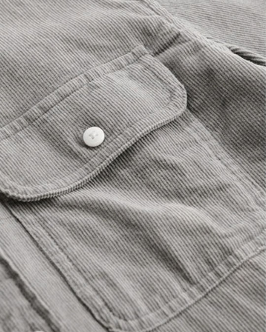 Close-up of a grey cotton corduroy shirt featuring a button-flap chest pocket and soft ribbed texture.