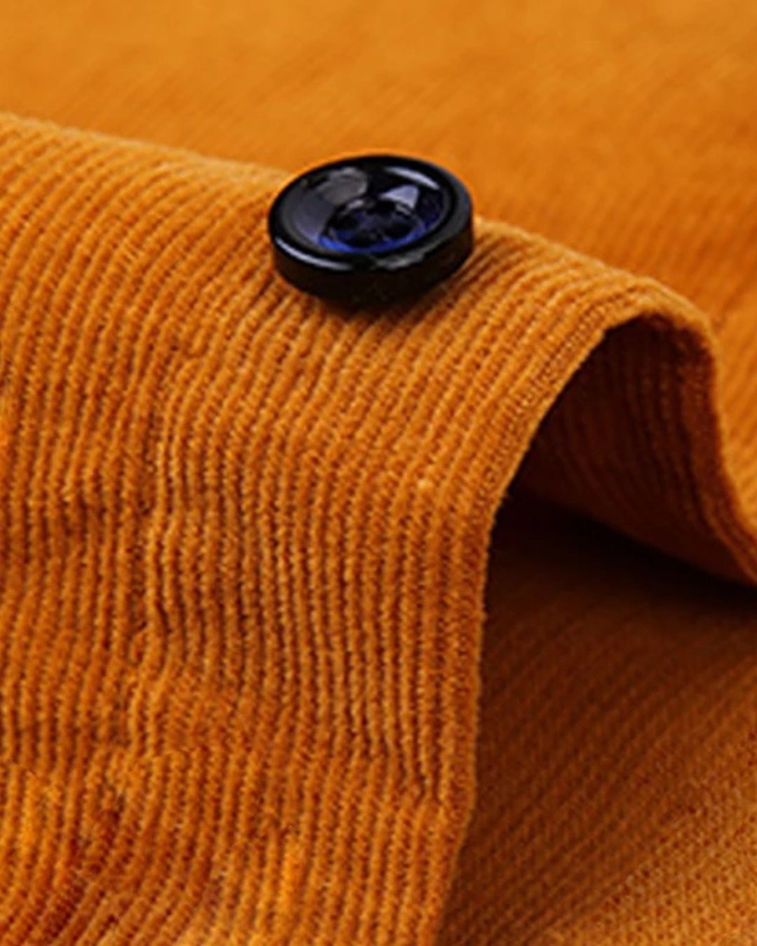 Close-up of a mustard yellow cotton corduroy shirt featuring a soft ribbed texture and a dark button detail.