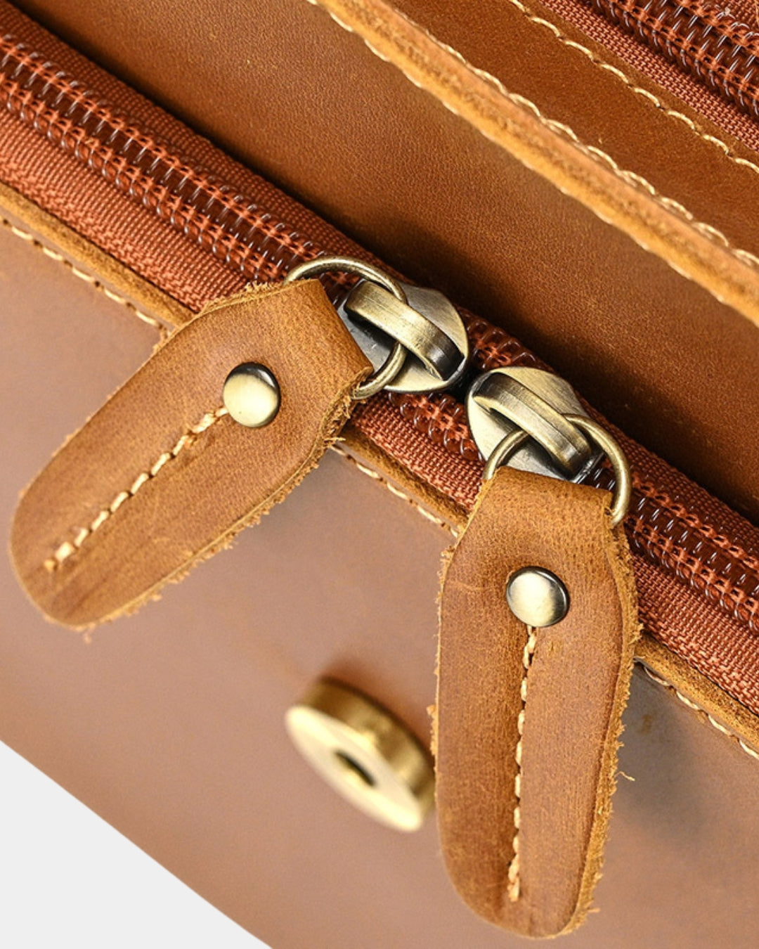 Close-up of a brown leather zippered pouch or clutch with matching leather pull tabs and metal zipper hardware.