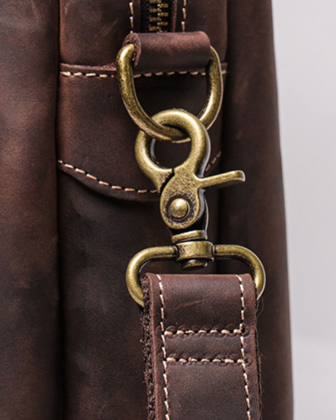 Close-up of a dark brown leather bag with an antique brass snap hook clasp and zipper detail.