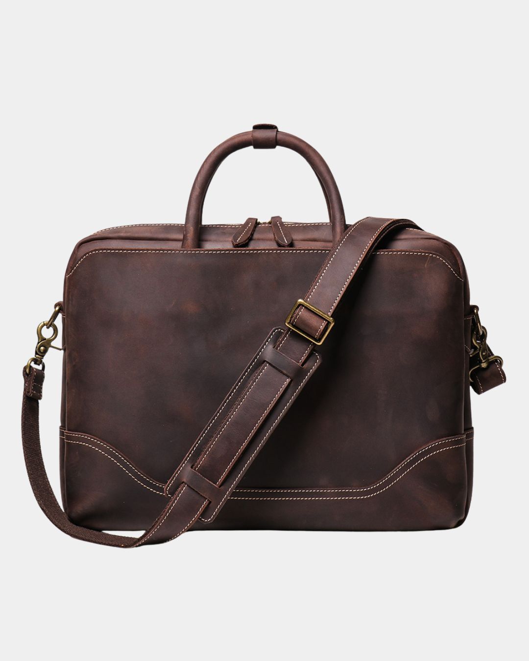 A dark brown distressed leather briefcase with a top handle, adjustable shoulder strap, and brass hardware, shown against a light gray background.