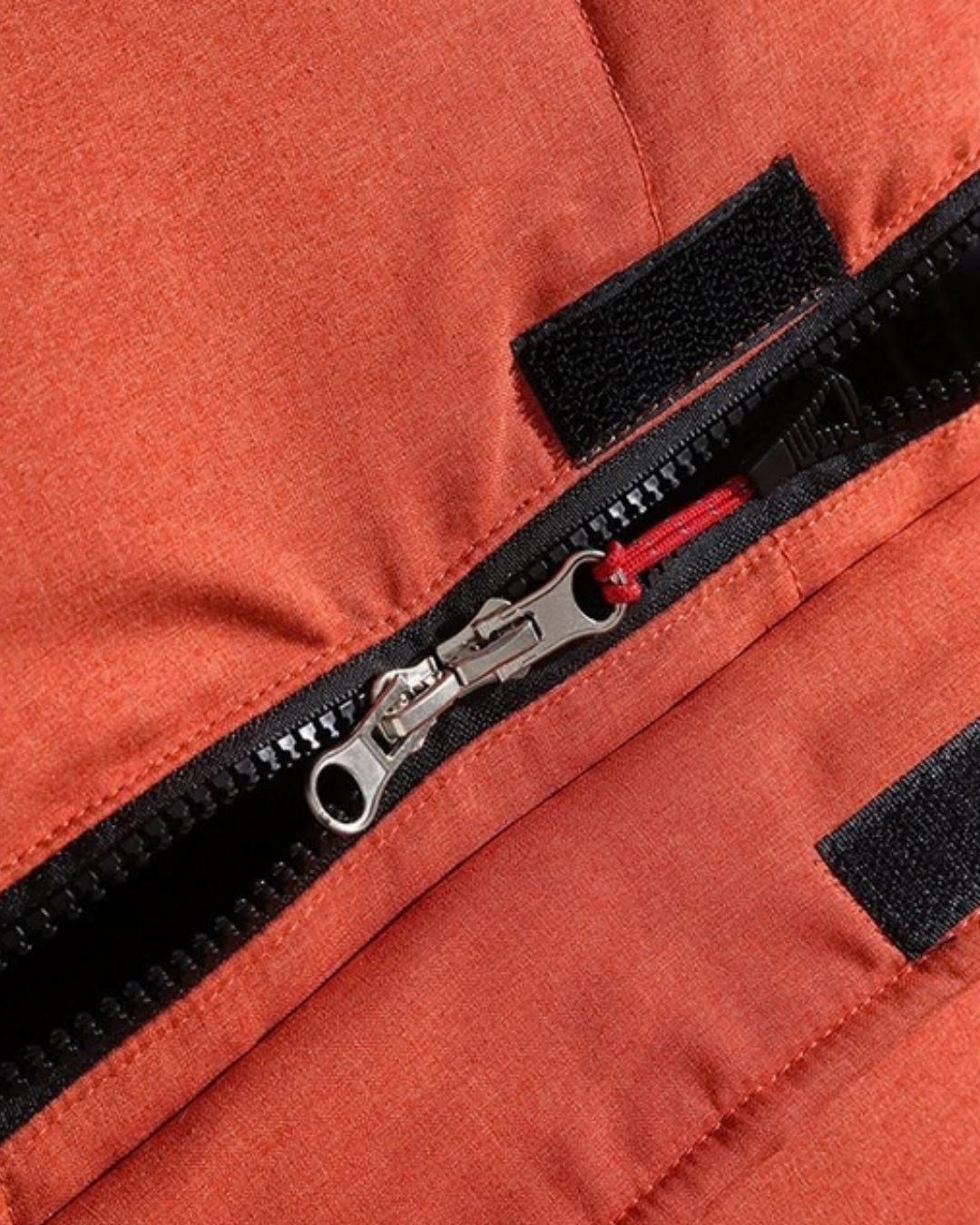 Close-up of a rust-orange puffer ski jacket featuring a durable front zipper, storm flap, and secure velcro closures.