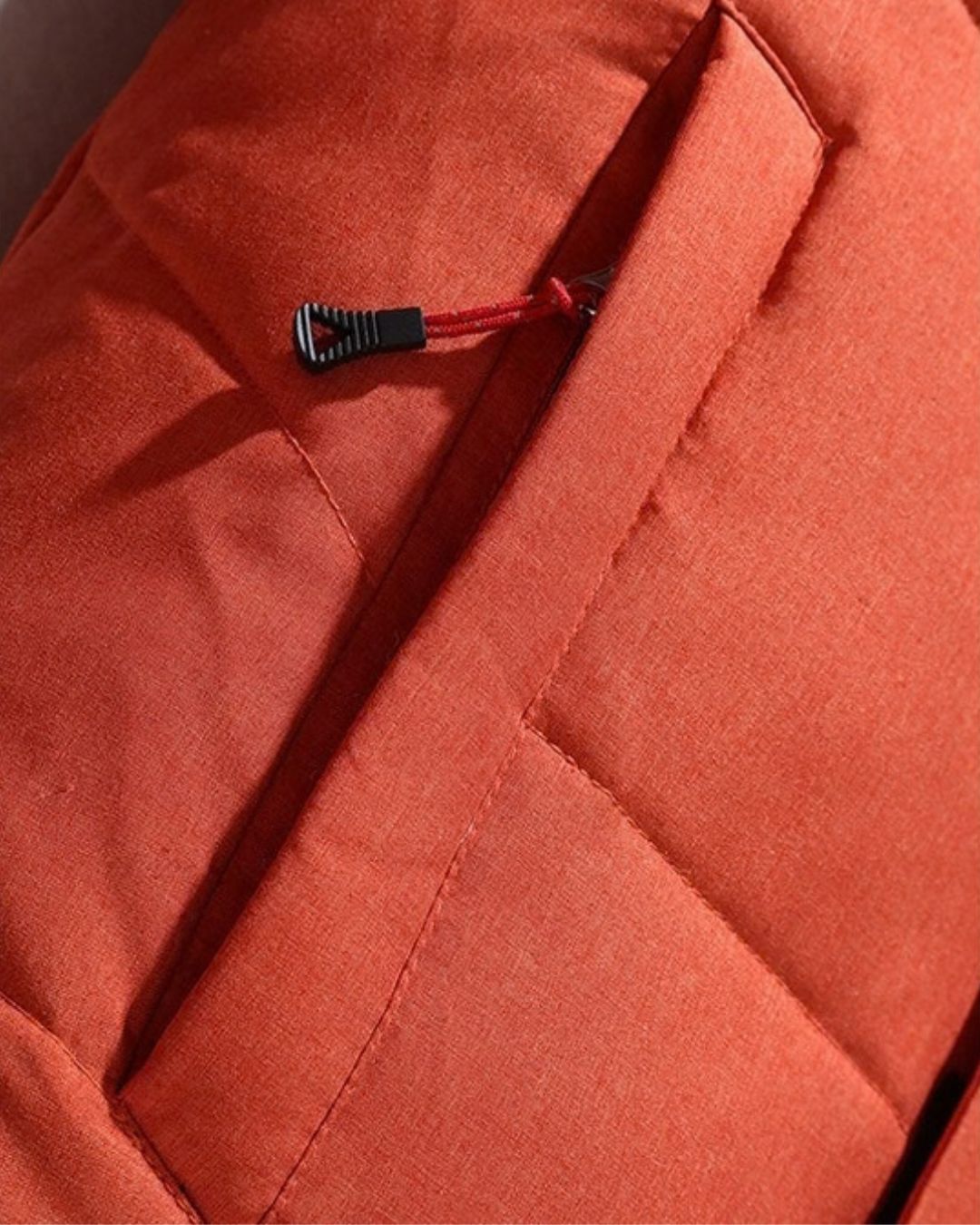 Close-up of a vibrant orange insulated puffer ski jacket featuring a secure zippered pocket with a textured pull tab.
