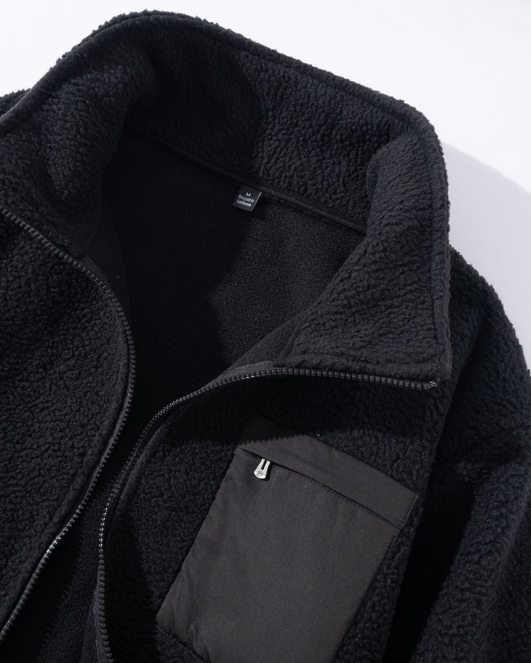 Black men’s full-zip teddy jacket in soft sherpa fleece with a high collar and a contrasting zippered chest pocket.